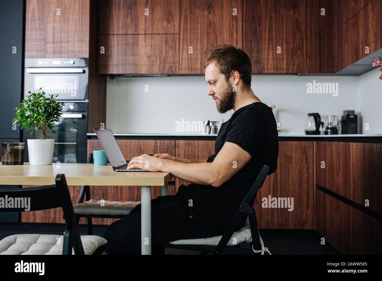 Vista laterale di un uomo che fa il lavoro freelance al tavolo da pranzo. Foto Stock