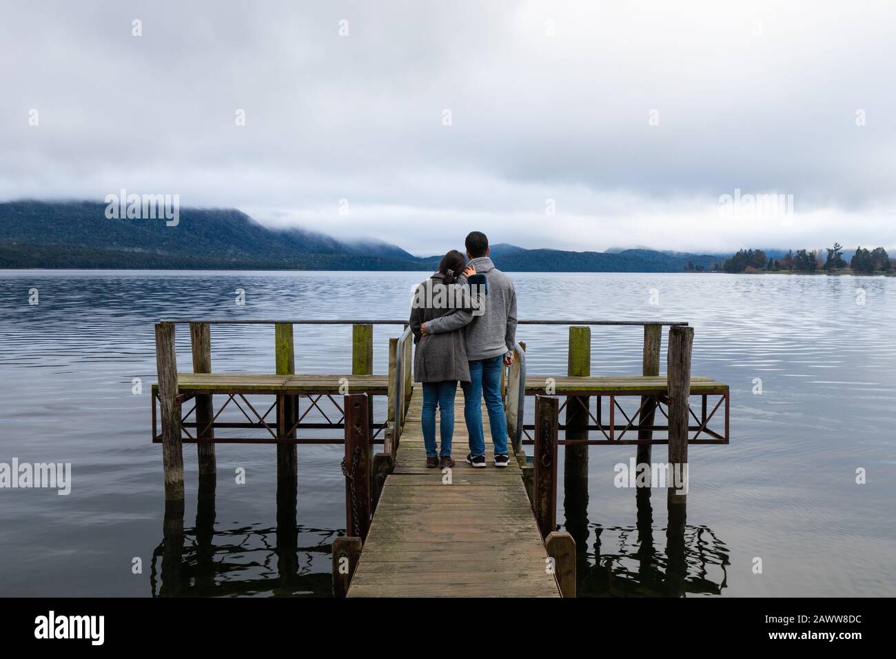 Giovane coppia asiatica abbracciando appoggiato alla spalla sul ponte Lago te Anau Nuova Zelanda Foto Stock