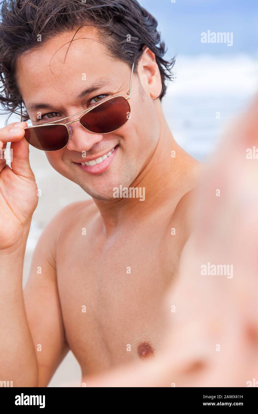 Attraente bel maschio asiatico biraciale sulla spiaggia vacanza indossando occhiali da sole sorridenti Foto Stock