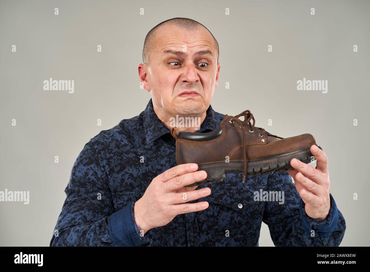 L'uomo caucasico che tiene una scarpa puzzolente con un'espressione di disgusto Foto Stock