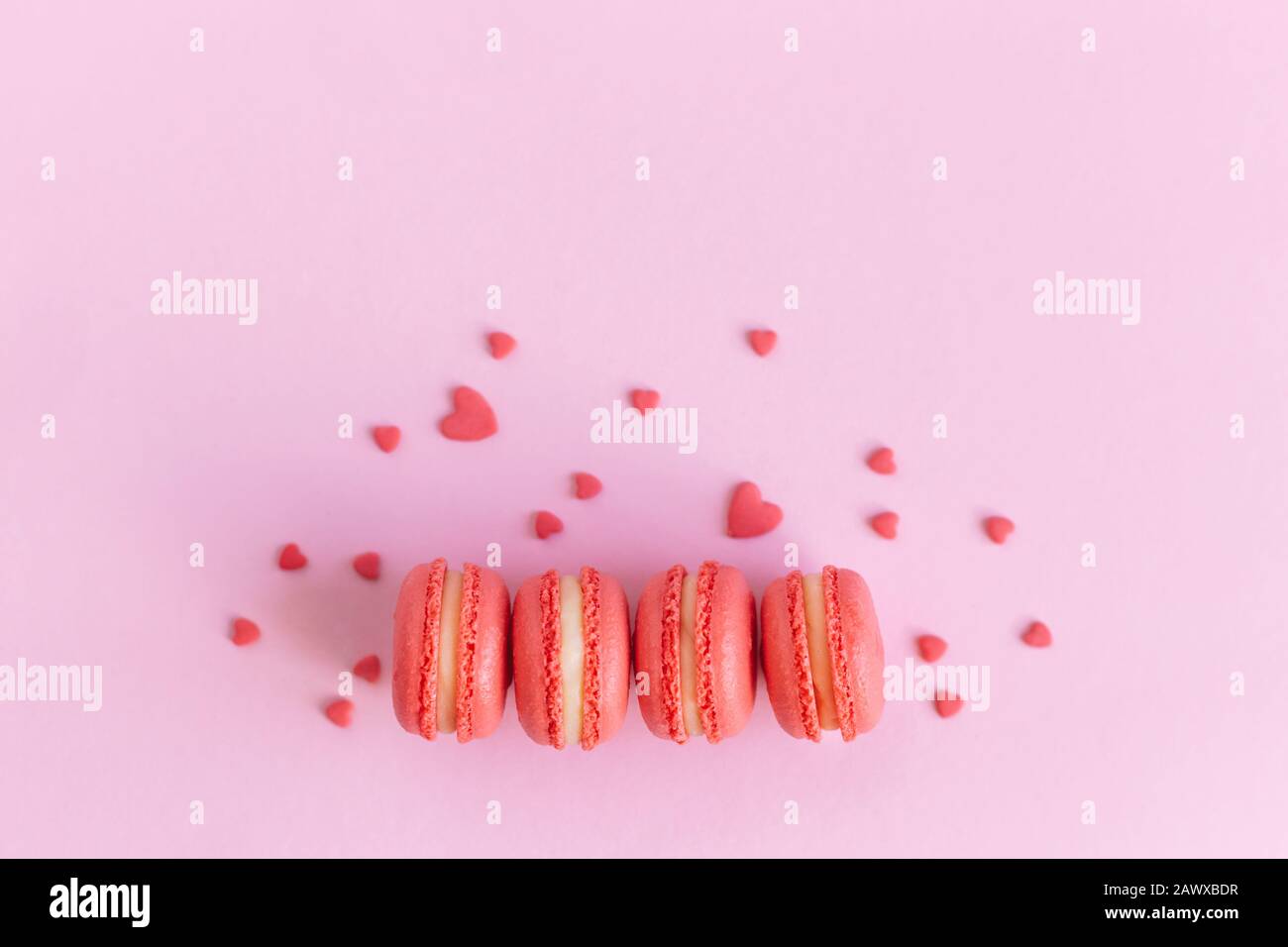 Gustosi amaretti francesi su sfondo rosa, decorati con cuori dolci. Concetto per San Valentino. Disposizione piatta. Inserire il testo. Foto Stock