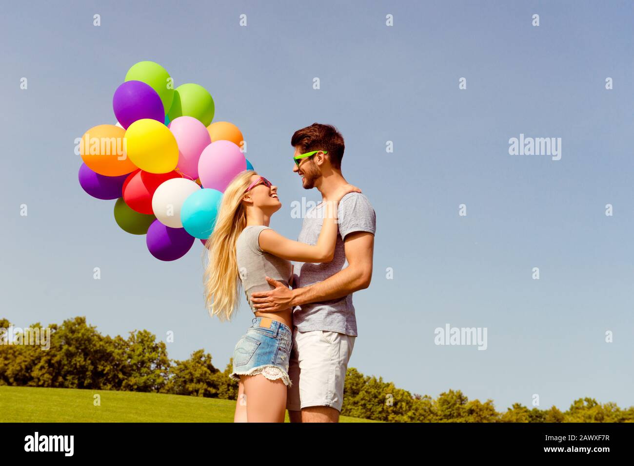 Giovane uomo felice abbracciando la sua ragazza e tenendo palloncini Foto Stock