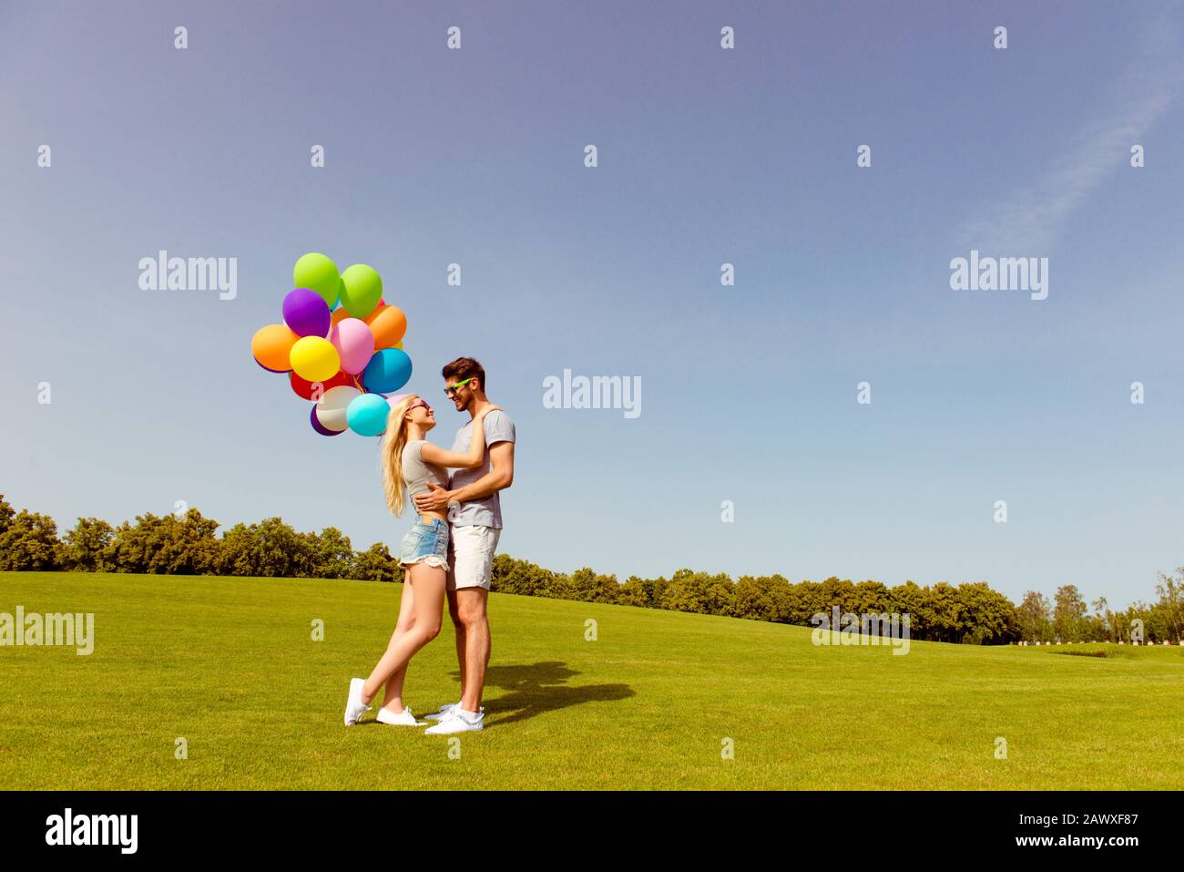 Due giovani amanti felici con palloncini che abbracciano nel parco Foto Stock