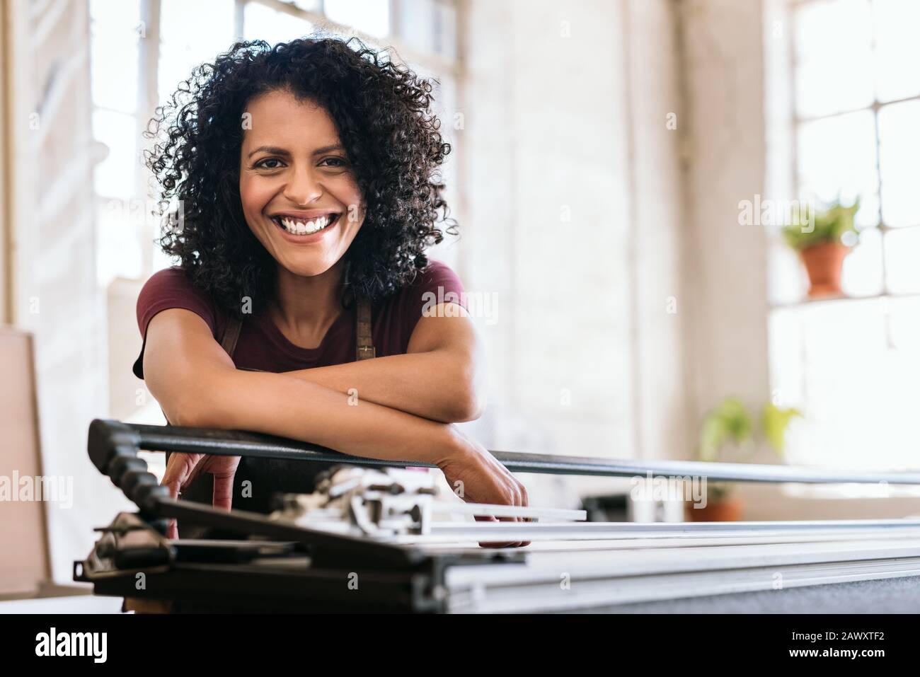 Giovane donna sorridente appoggiata su un banco da lavoro nel suo studio Foto Stock