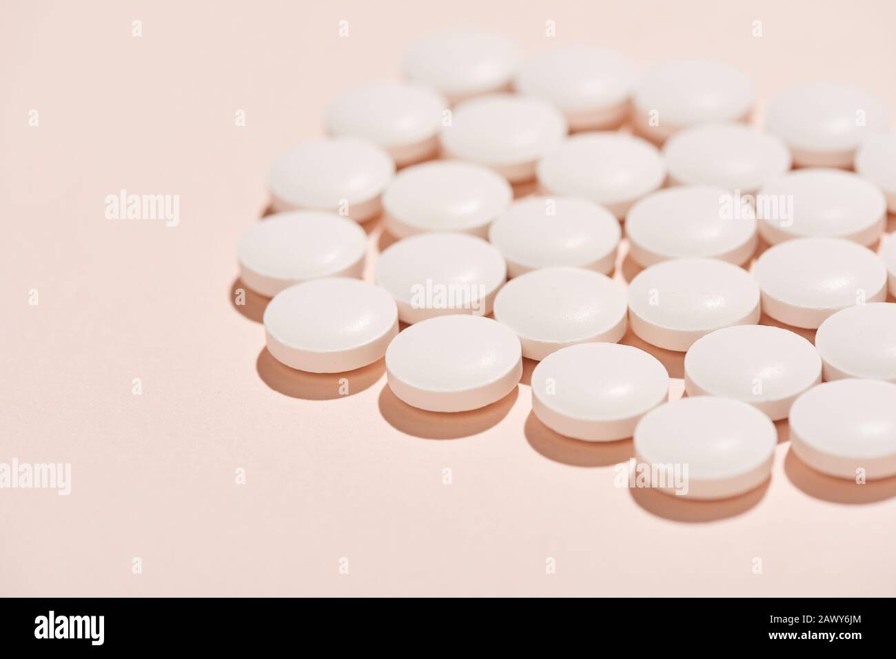 Pillole bianche della stessa forma su sfondo rosa pallido orizzontale primo piano Foto Stock