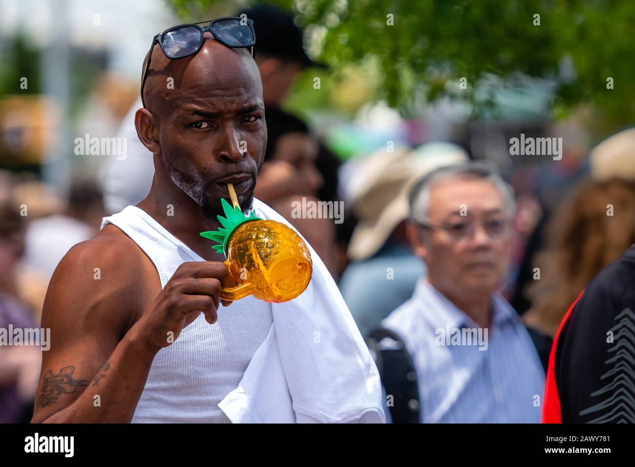 Brooklyn, New York City, USA - 22 giugno 2019: Sfilata annuale delle sirene delle Coney Islands, un uomo africano si leva in piedi in una folla e beve una bevanda rinfrescante Foto Stock