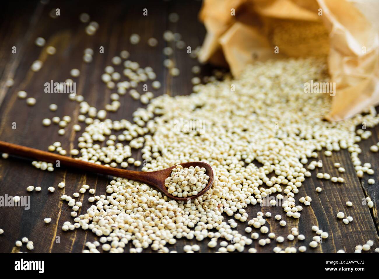 Cucchiaio di legno con grano di sorgo e cucchiaio su tavola di legno scuro. Sacchetto di carta sullo sfondo Foto Stock