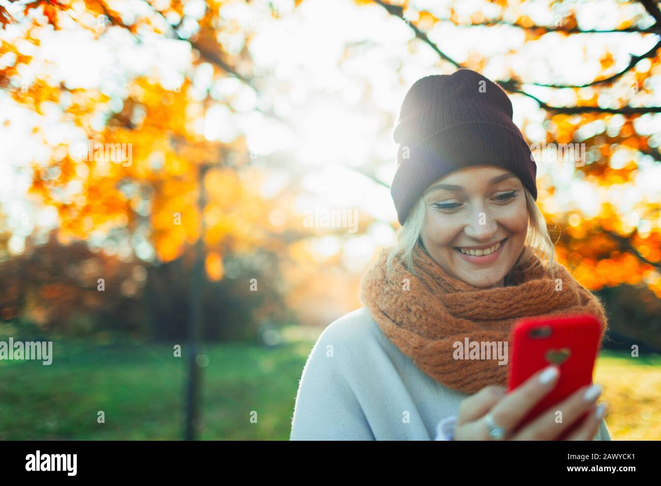 Donna sorridente con smartphone nel soleggiato parco autunnale Foto Stock