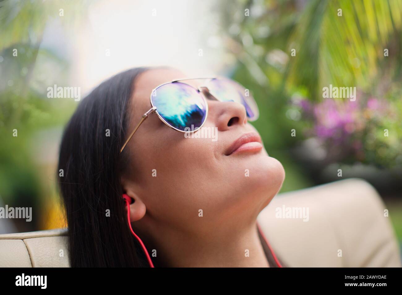 Chiudete la serena donna con gli occhiali da sole, ascoltando la musica con le cuffie Foto Stock