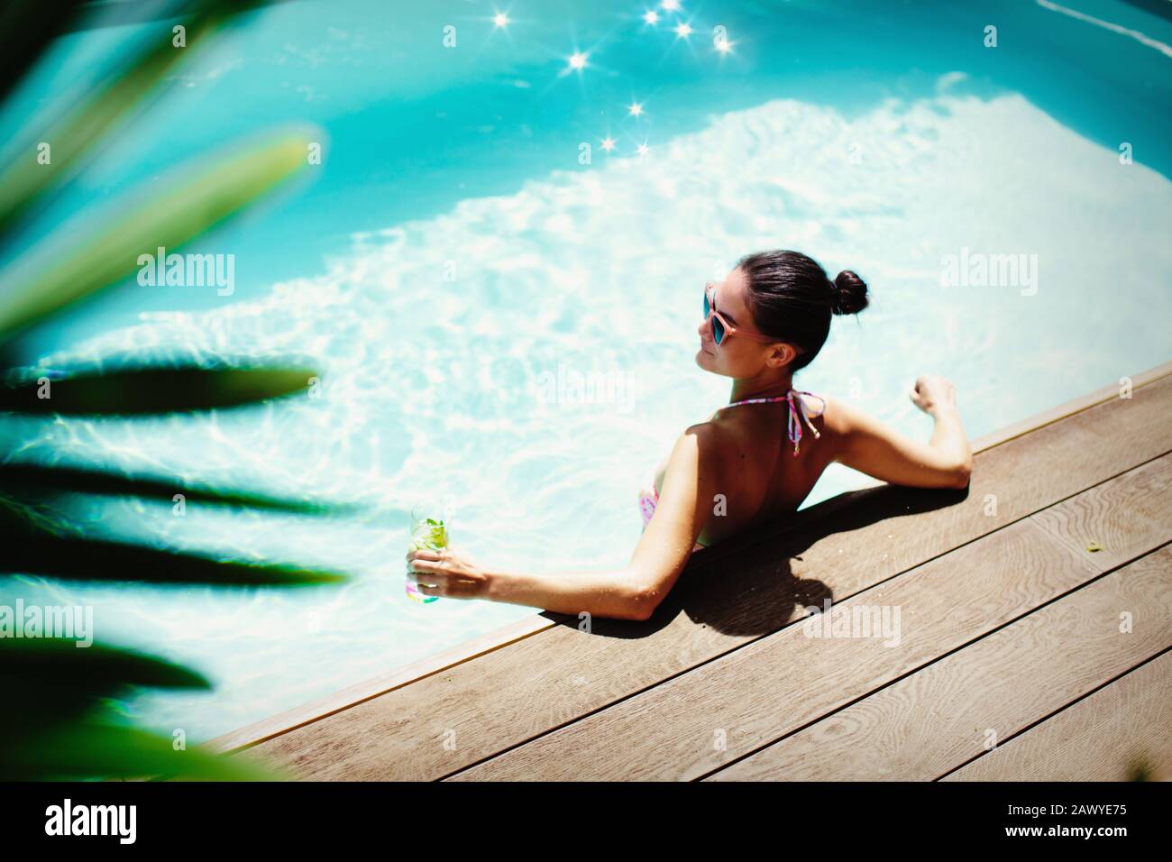 Donna rilassante con cocktail nella soleggiata piscina estiva Foto Stock