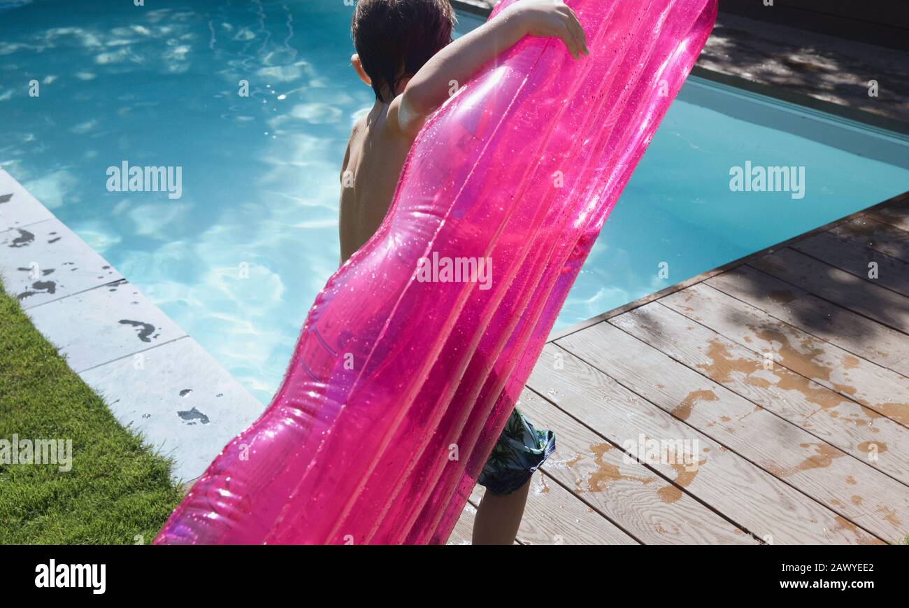 Ragazzo con zattera gonfiabile rosa al sole estate a bordo piscina Foto Stock