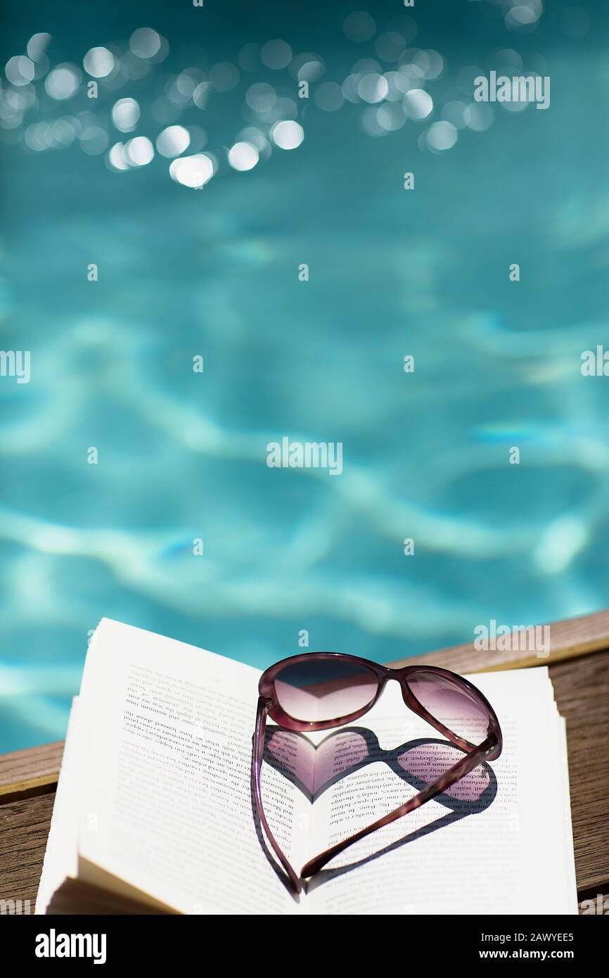 Occhiali da sole a forma di cuore a libro presso la soleggiata e idilliaca piscina estiva Foto Stock