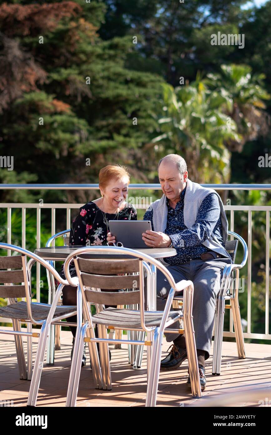 Coppia in pensione seduti sulla terrazza all'aperto con un computer portatile che si gode il loro tempo libero Foto Stock