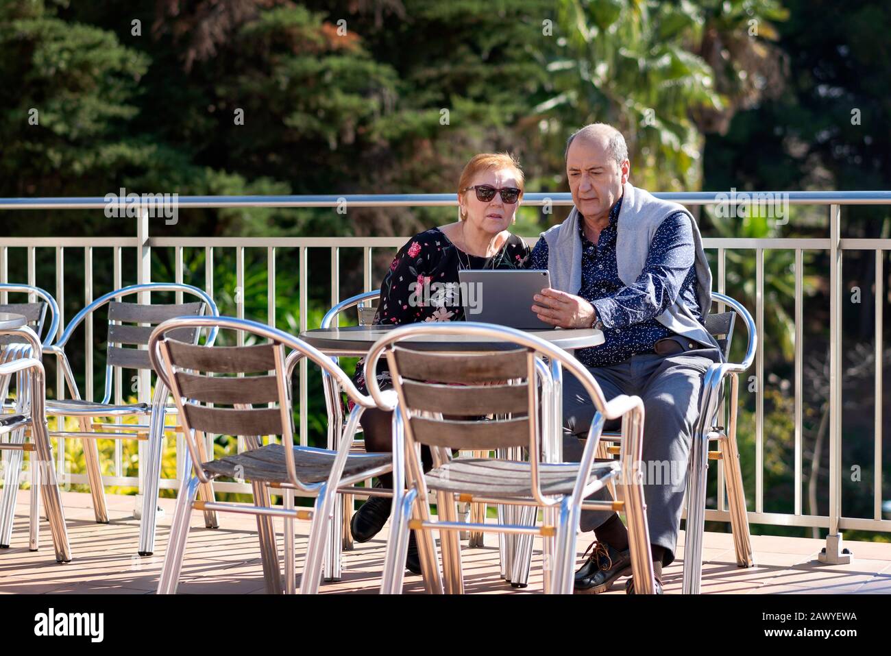 Coppia in pensione seduta sulla terrazza all'aperto che guarda preoccupato per il portatile Foto Stock