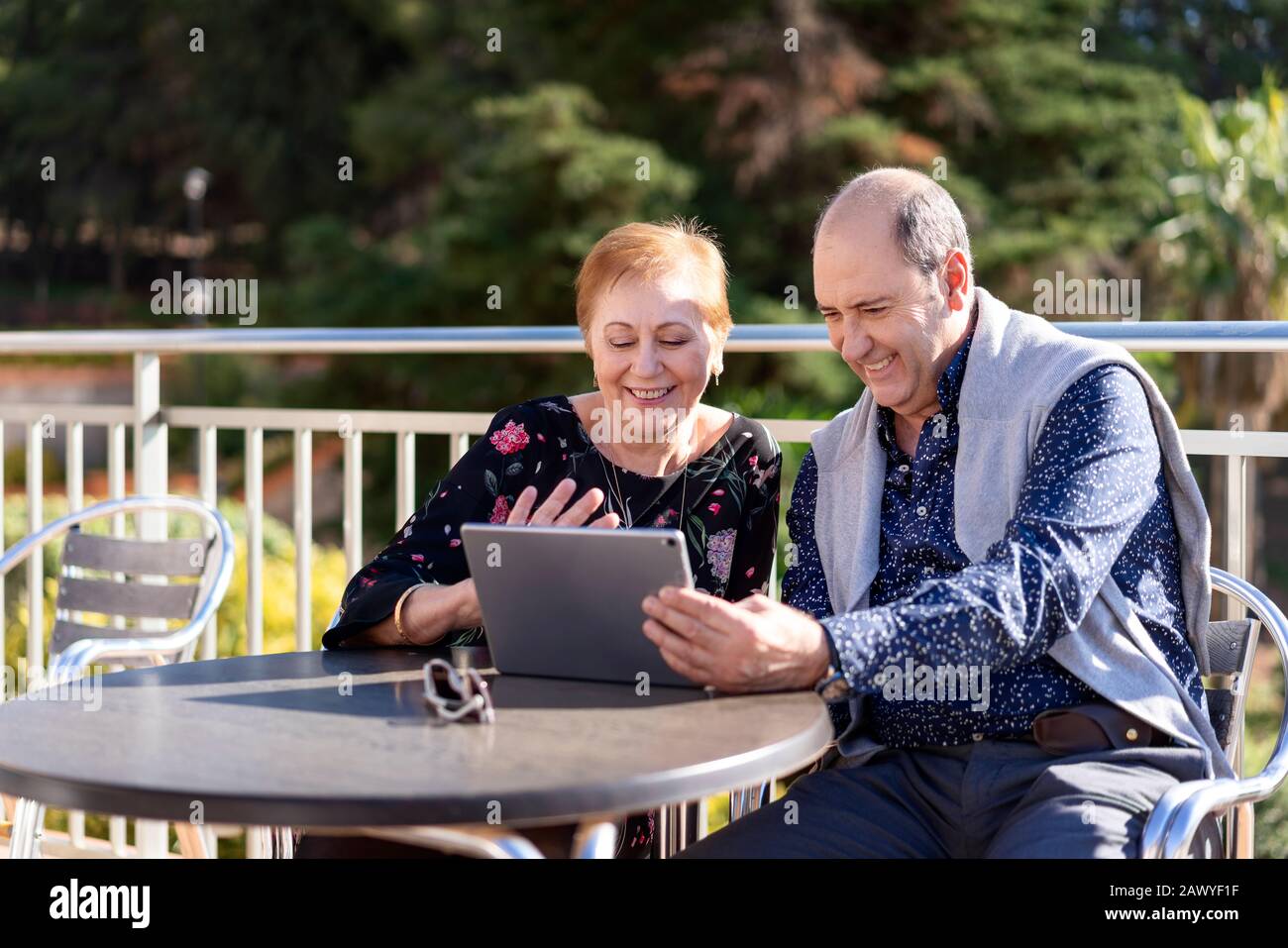 Coppia in pensione seduti sulla terrazza all'aperto con un computer portatile che si gode il loro tempo libero Foto Stock