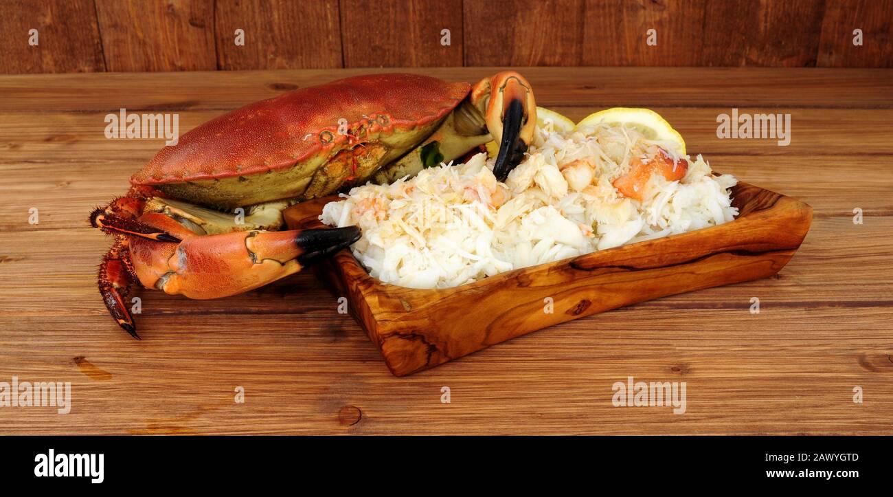 Granchio marrone fresco cotto e carne fresca in un piatto di legno su uno sfondo di legno con limone Foto Stock