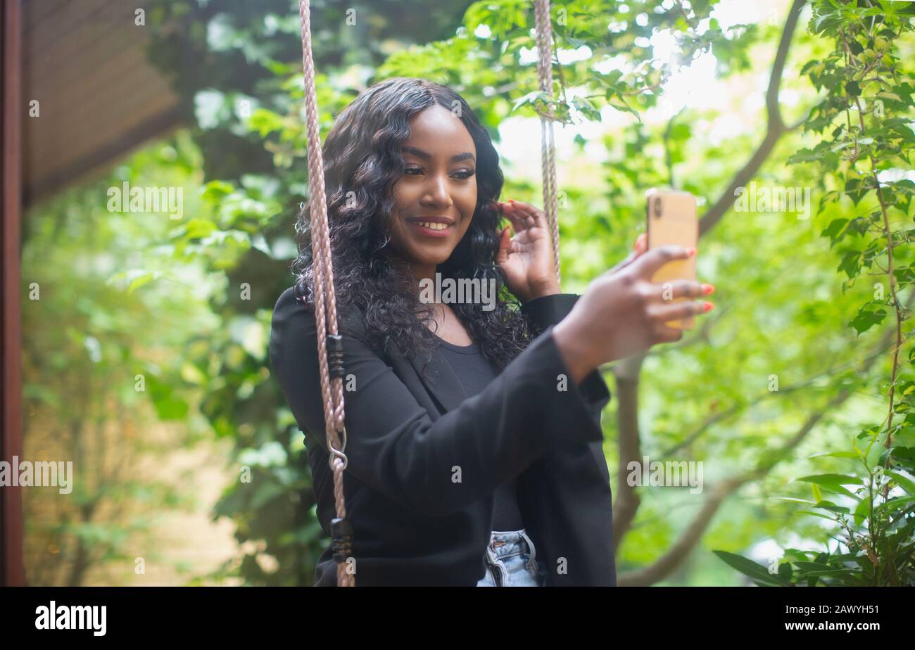 Giovane donna con macchina fotografica telefono posa per selfie sul patio swing Foto Stock