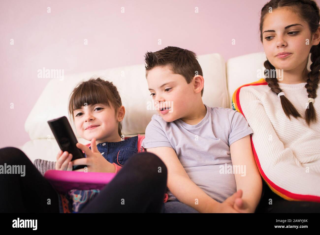 Sorelle e fratello con sindrome Di Down guardare la TV sul divano Foto Stock