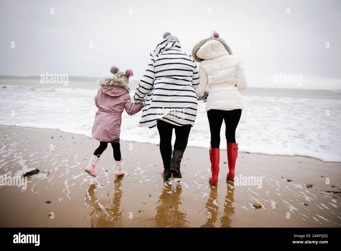 Madre e figlie in abiti caldi a piedi sulla spiaggia dell'oceano invernale Foto Stock