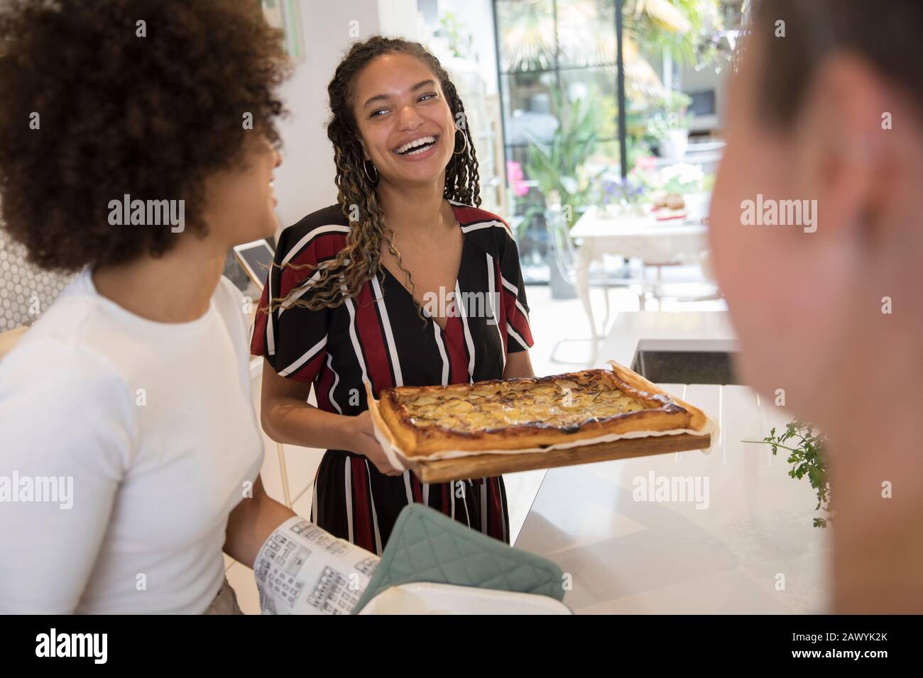 Felice giovane donna che serve pizza fatta in casa ad amici in cucina Foto Stock