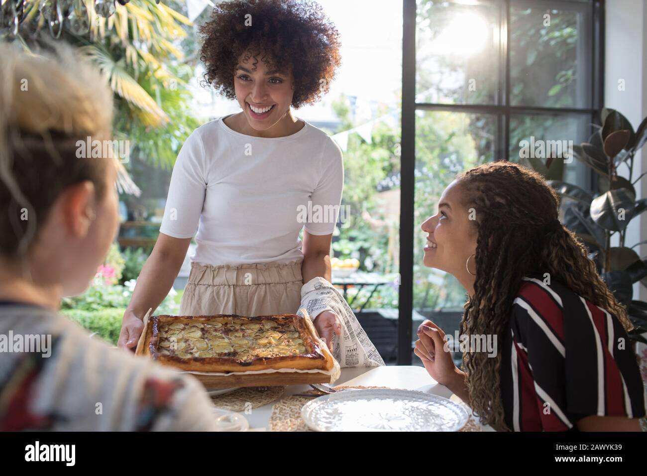 Giovane donna che serve pizza fatta in casa agli amici al tavolo da pranzo Foto Stock