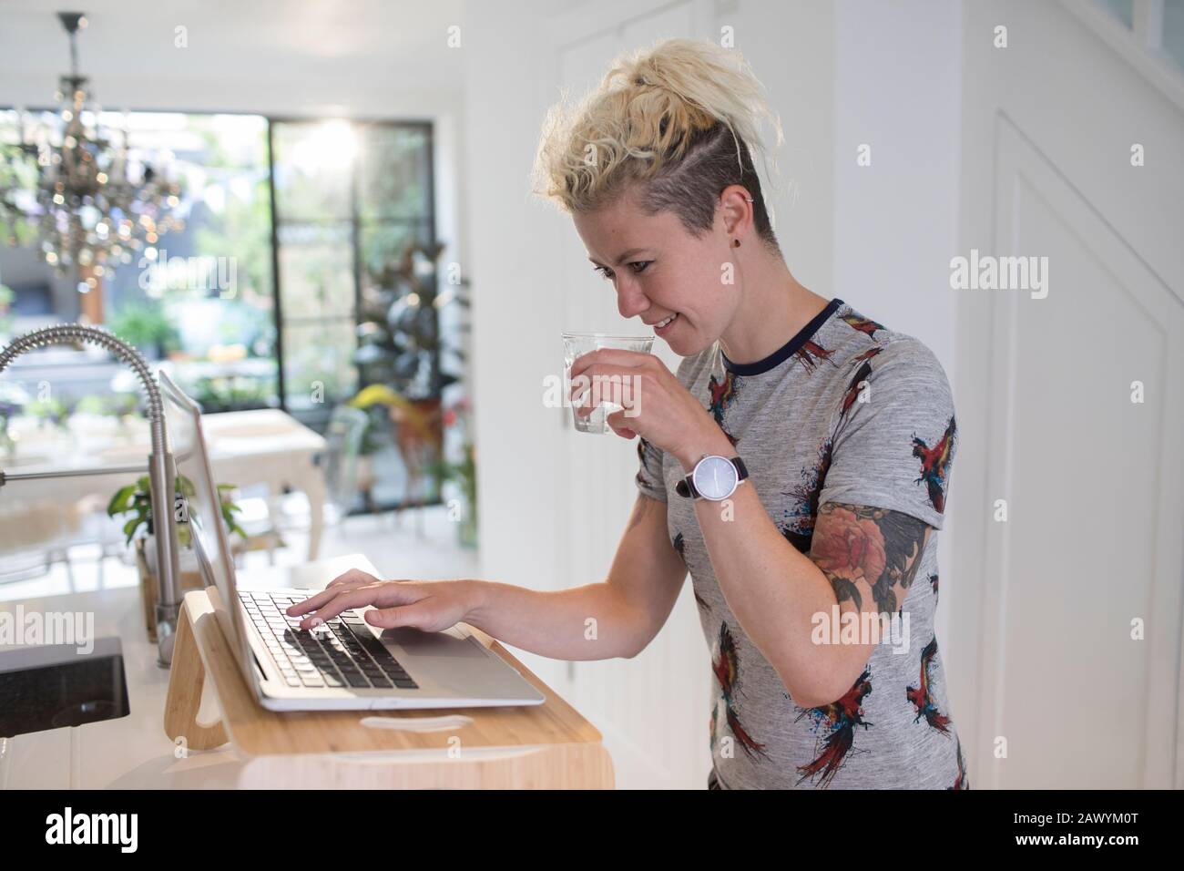 Donna che beve acqua e che lavora a computer portatile in cucina Foto Stock