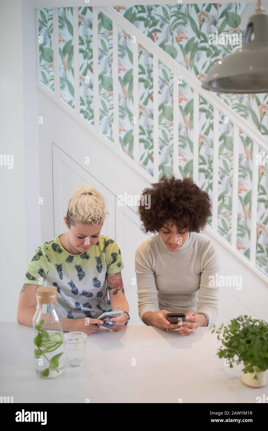 Giovani amici donne che utilizzano smartphone in cucina Foto Stock
