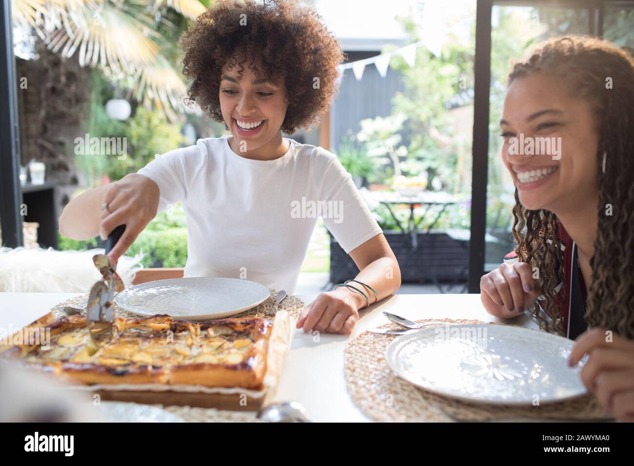 Felici giovani amici donne affettare pizza fatta in casa a tavola Foto Stock