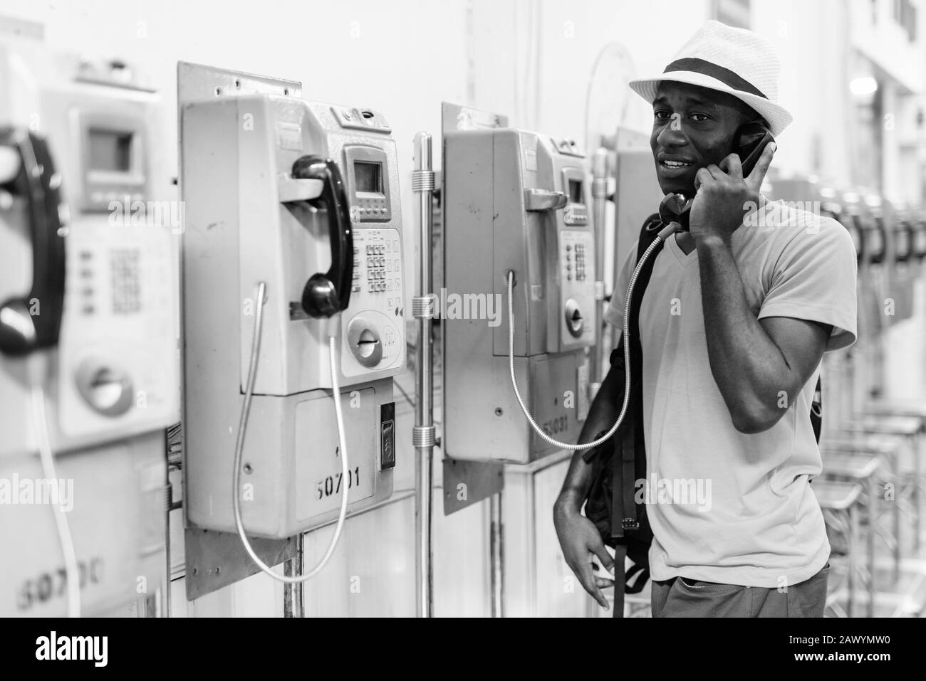 Giovane felice turista africano sorridente mentre parla sul telefono a pagamento all'interno della stazione ferroviaria Foto Stock