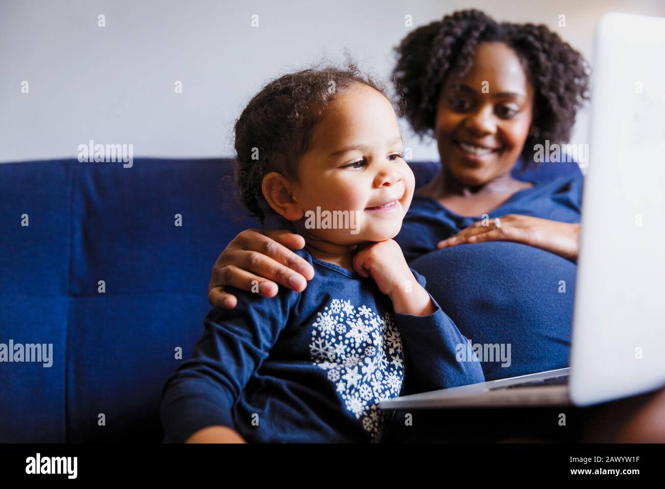 Madre incinta felice e figlia prescolare usando il laptop sul divano Foto Stock