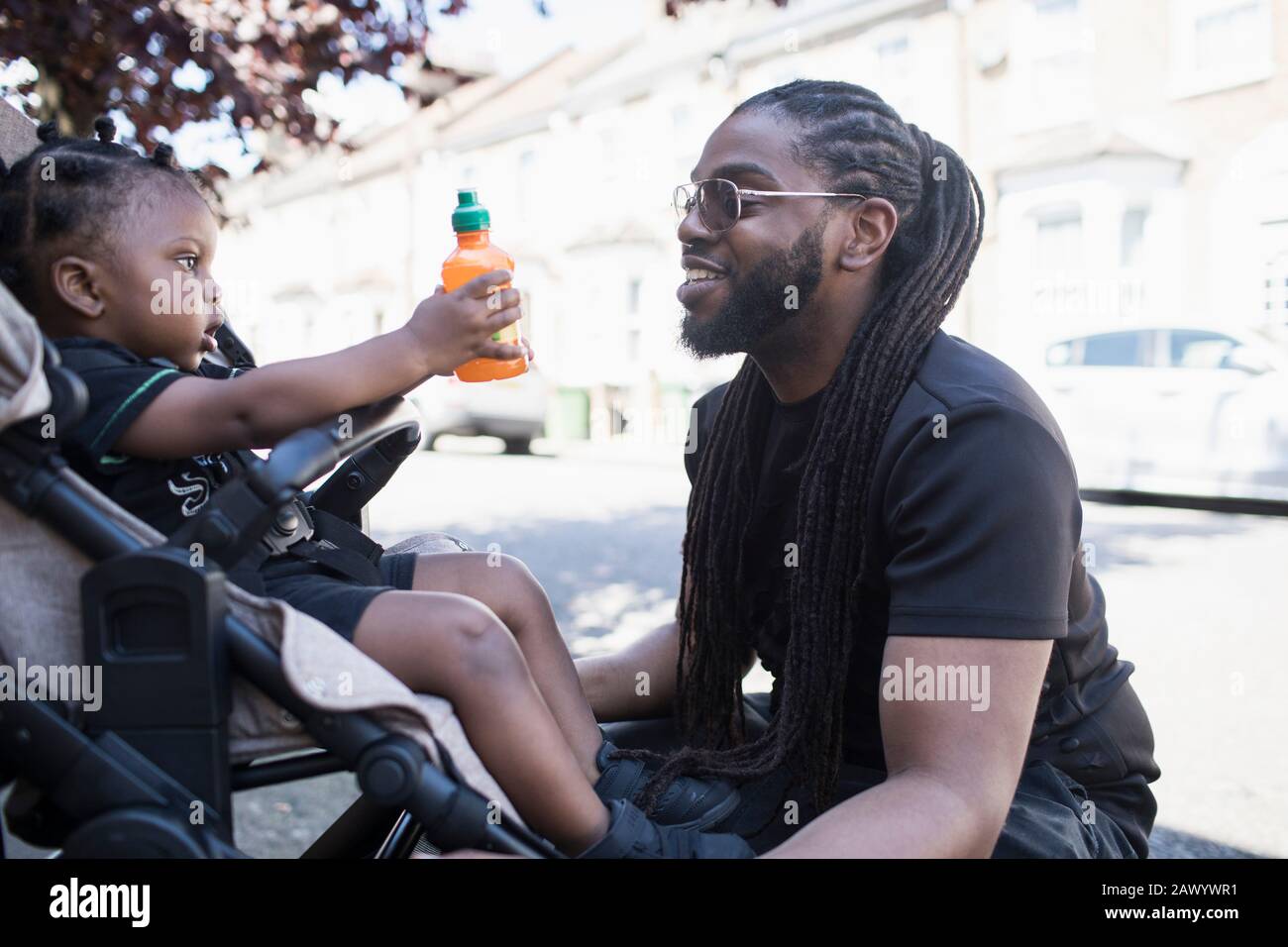 Padre parlando con il figlio bambino in passeggino sul marciapiede urbano Foto Stock