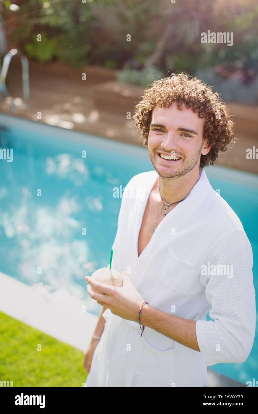 Ritratto giovane felice in accappatoio bevendo dalla noce di cocco a bordo piscina Foto Stock