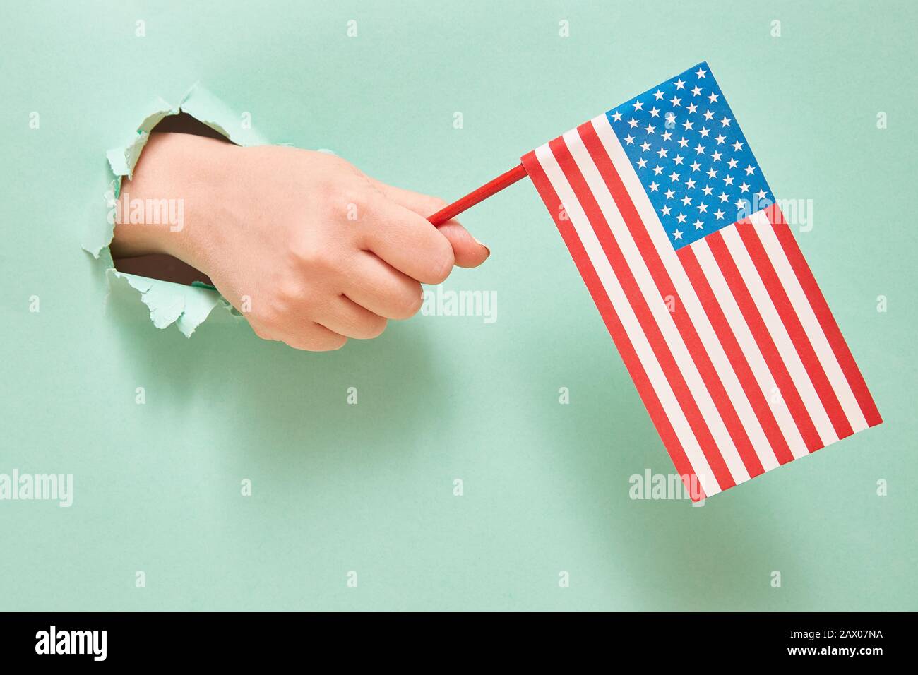 Una mano da un buco in carta verde tiene una bandiera americana con stelle blu. Concetto Del Giorno Dell'Indipendenza Dell'America. Spazio di copia Foto Stock