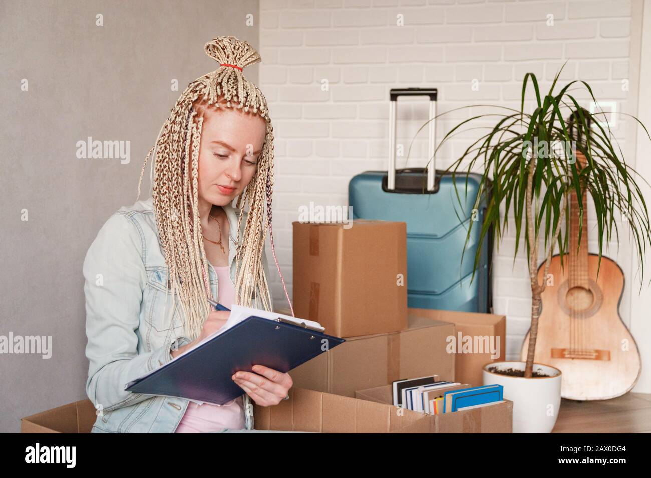 Bella donna in abiti casual è impacchettare il suo roba nelle scatole, prendendo appunti Foto Stock