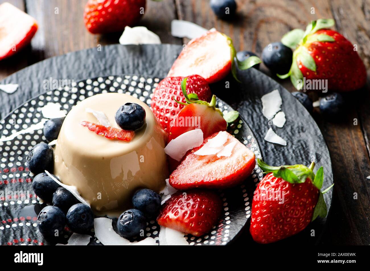 Tradizionale dessert italiano panna cotta, decorato con fragole e mirtilli su un piatto primo piano, fuoco selettivo Foto Stock