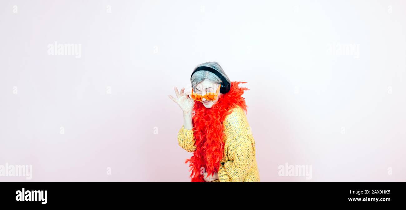 felice anziano ritratto donna con occhiali da sole cuffie musica e boa rosso - giovane e divertente stile di vita terza età Foto Stock