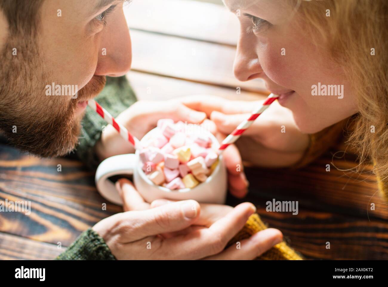 Giovane coppia bevendo cioccolata calda con marshmallows a forma di cuore usando cannucce da bere di carta. Data di San Valentino Foto Stock