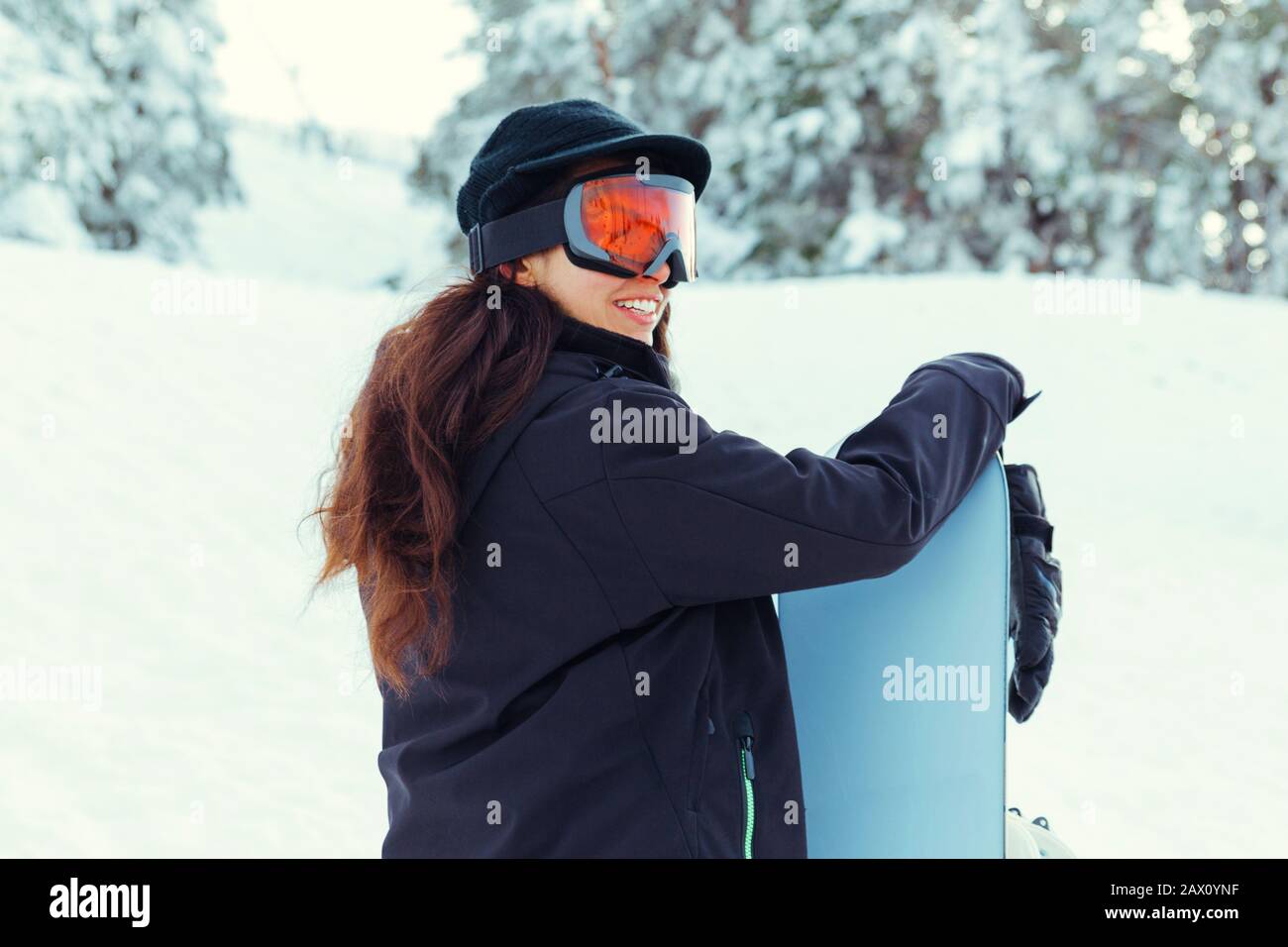 Foto di scorta di una giovane ragazza che ride mentre tiene il suo snowboard su una montagna innevata Foto Stock