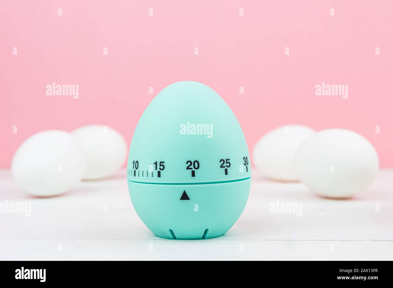 Cucina blu uovo timer su sfondo rosa. Tempo di cottura, presto Pasqua. Uova di gallina bianca. Copia spazio Foto Stock