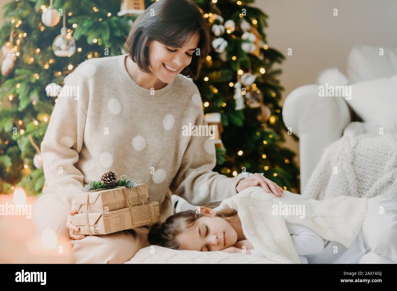 Ho poco segreto per te. Madre e figlia adorabili celebrano il nuovo anno a casa. La mamma pone vicino alla ragazza del sonno con regali contro decorato nuovo Foto Stock