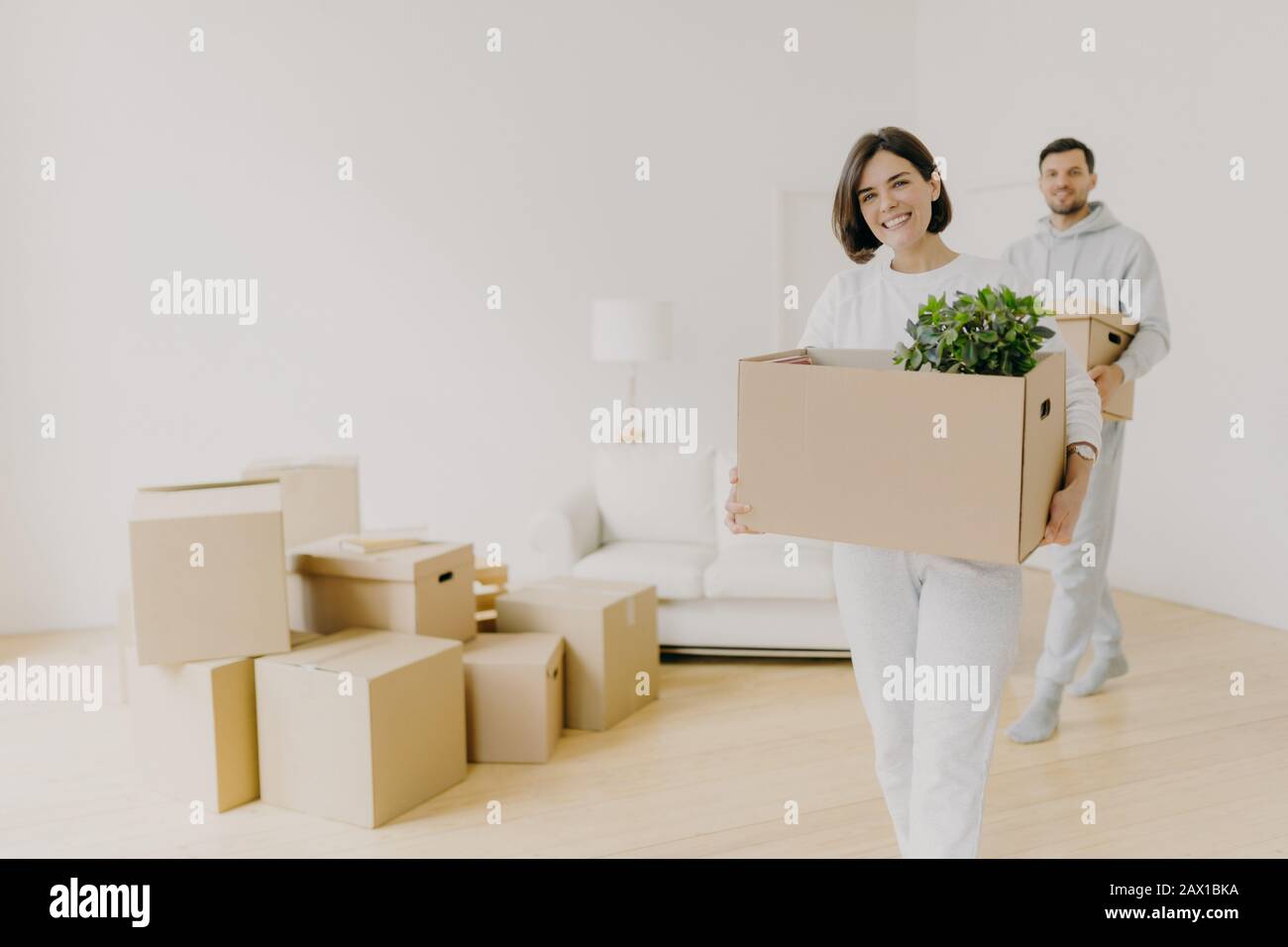 La donna felice e suo marito portano le scatole con gli effetti personali, essendo occupato durante la rilocazione in altro posto per vivere, entrare in nuova casa, spostare insieme Foto Stock