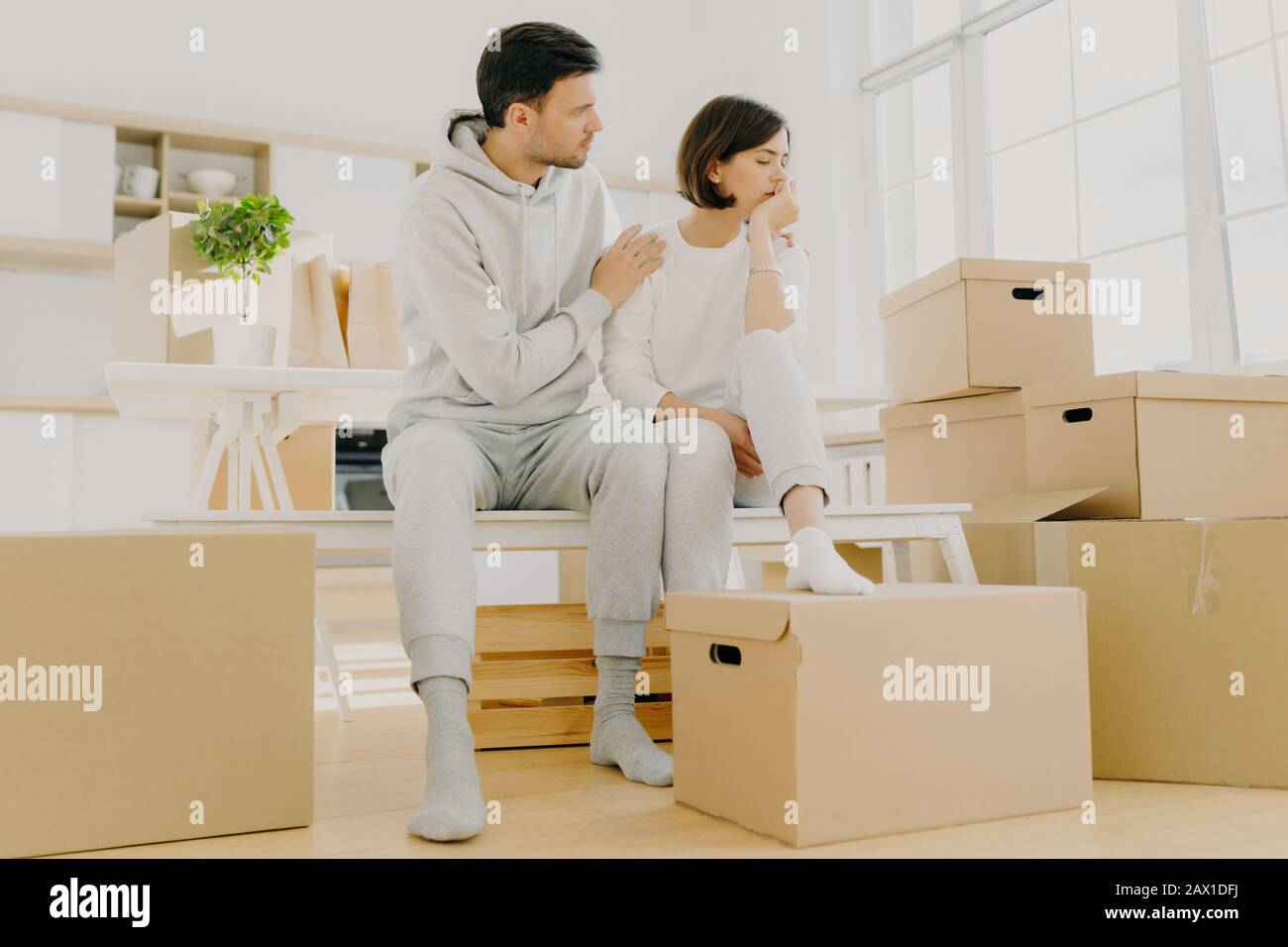 Indoor shot di frustrato donna e uomo affrontare problemi finanziari, sedersi su panca in spazio vuoto spazioso, disimballare scatole di cartone con roba personale. Cari Foto Stock