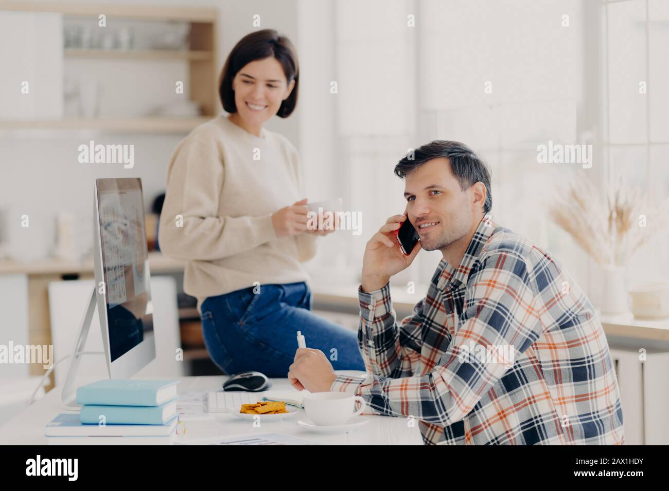 Piacere marito e moglie gestire le finanze a casa, rivedere conti bancari, l'uomo contento tiene il cellulare vicino all'orecchio, indossa la camicia da passera, donna felice si siede Foto Stock