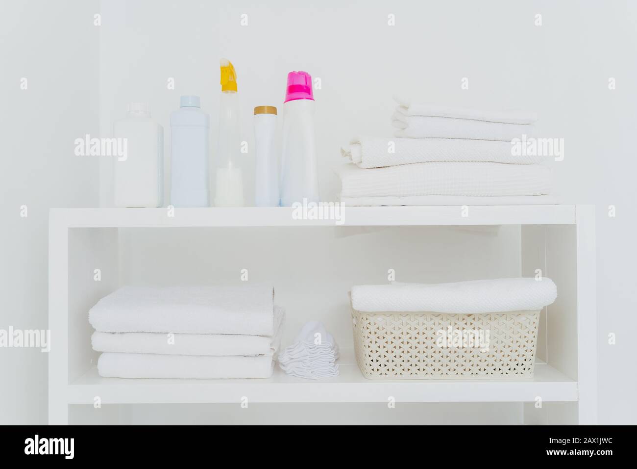 Lavanderia con asciugamani ben piegati, bottiglie di detersivo liquido o detersivi. Tutto in colori bianchi. Tutti i giorni faccende e lavanderia giorno Foto Stock