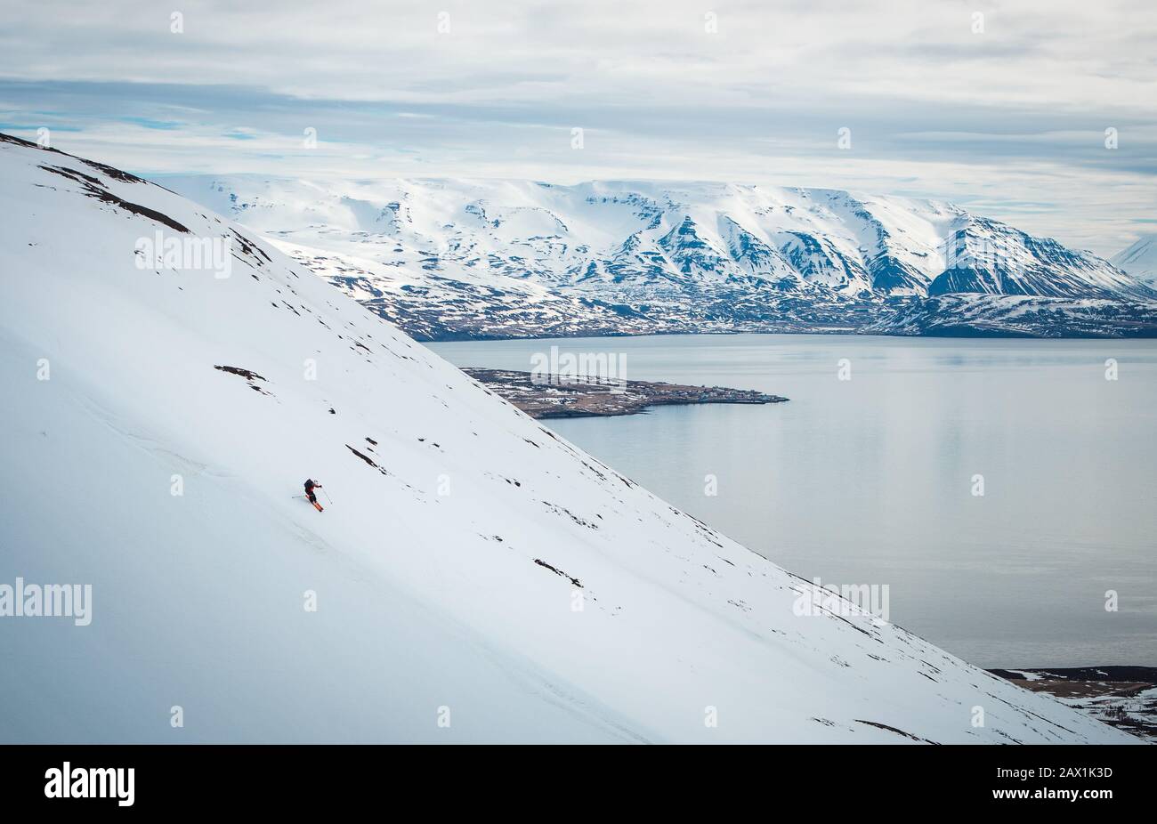 Un uomo che scia giù una montagna con montagne innevate e oceano dietro Foto Stock