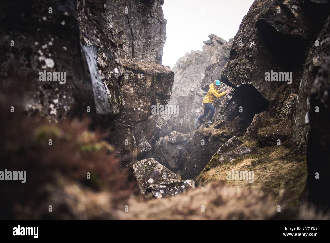 Donna in giacca gialla che esplora fessure termali in Islanda Foto Stock