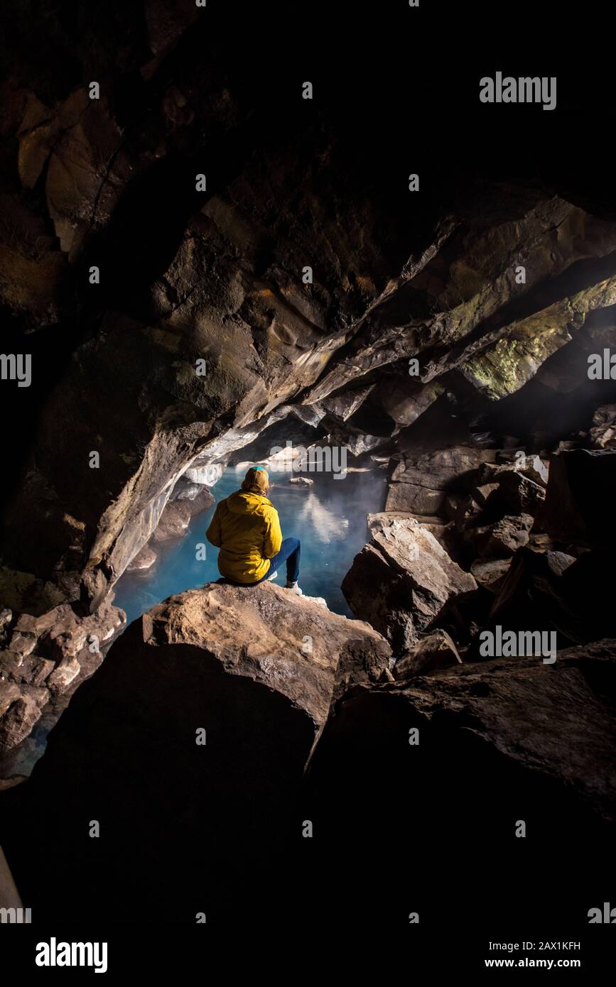 Donna seduta di fronte alla piscina termale in grotta Foto Stock