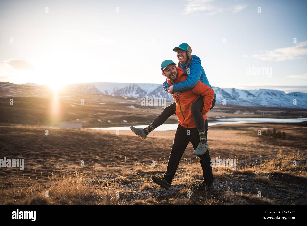 Uomo che porta donna su piggyback in campo con montagne sullo sfondo Foto Stock