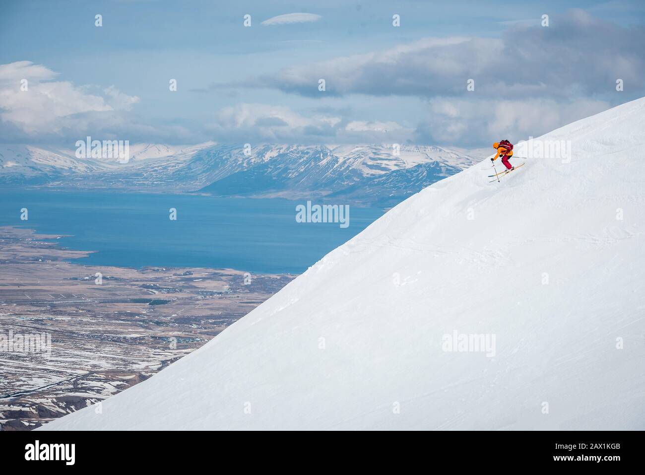 Un uomo salta su una montagna in Islanda con acqua dietro Foto Stock