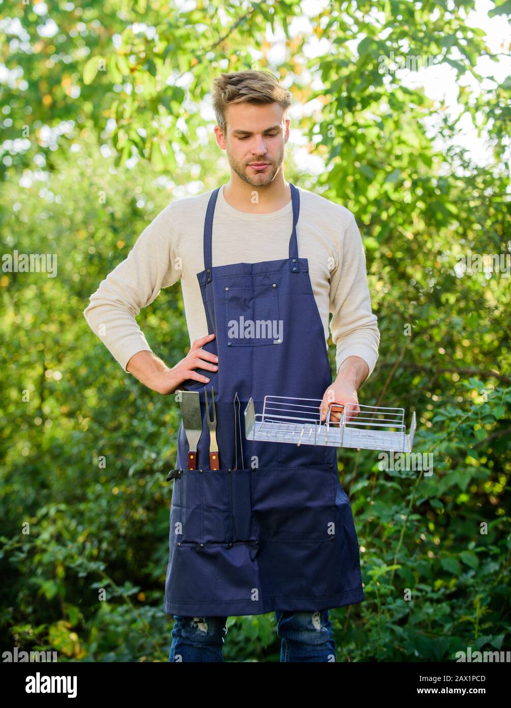 Attrezzi per tostare carne all'aperto. Metodi di cottura alla griglia. Barbecue concetto. Bel ragazzo che cucina cibo. Griglia grigliata MAN Hold. Grigliare gli alimenti. Cortile barbecue p Foto Stock